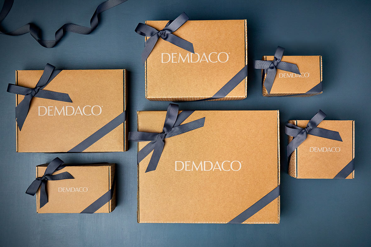 Brown boxes elegantly wrapped in dark ribbon and white DEMDACO sticker. Blue patterned notecard with the word Thankful printed on the front.